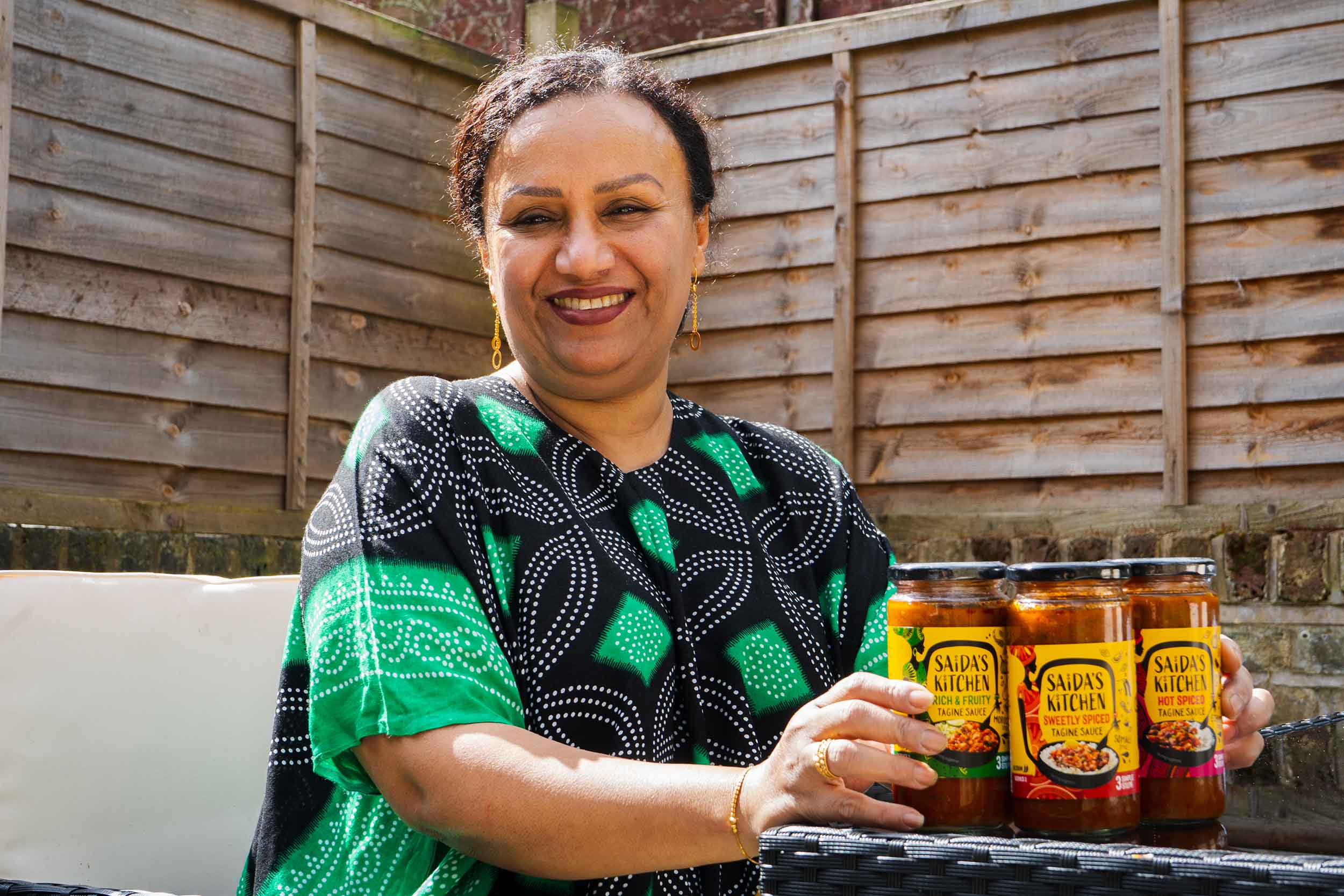 Saida smiling in her garden with the three Saida's Kitchen tagine sauces