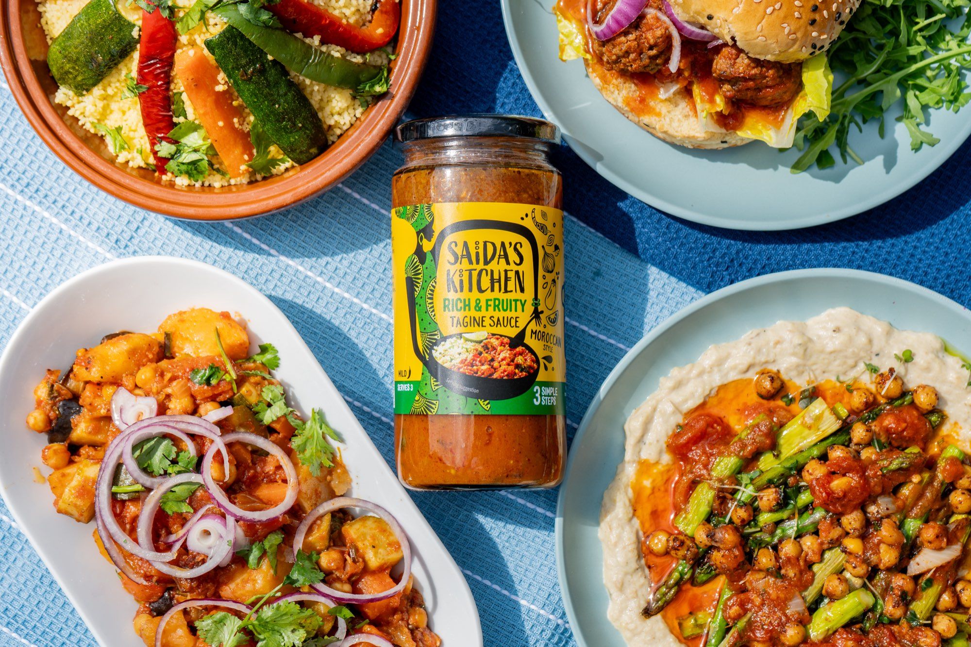 Overhead spread of Moroccan style dishes around a jar of Rich & Fruity Ras el Hanout tagine sauce